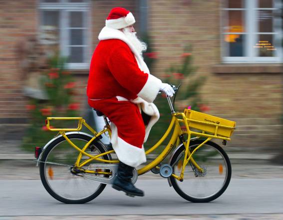 epa03987692 A man wearing a Santa Claus costume rides a bicycle to the Christmas post office in Himmelpfort, Germany, 12 December 2013. About 185,000 Christmas letters coming from all over the world were mailed to the post office so far. All letters arrived before 15 December 2013 will be answered.  EPA/PATRICK PLEUL